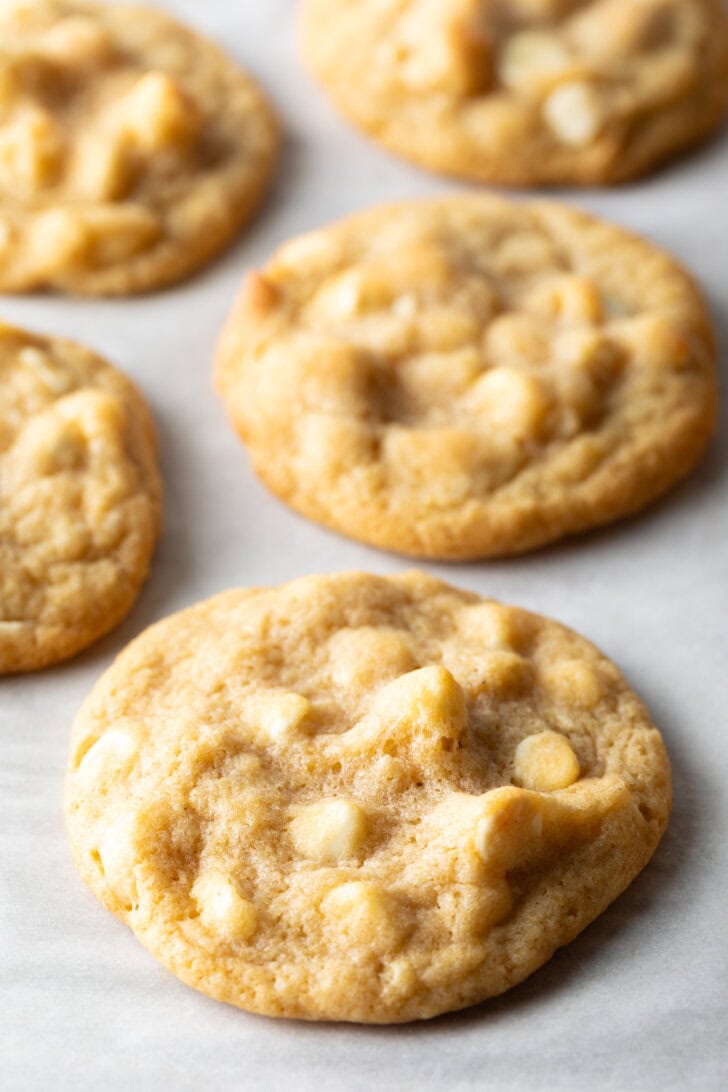 Close up view of three white chocolate macadamia nut cookies on parchment.